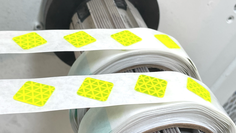 Rolls of pressure-sensitive adhesive labels on a die-cutting press spindle.