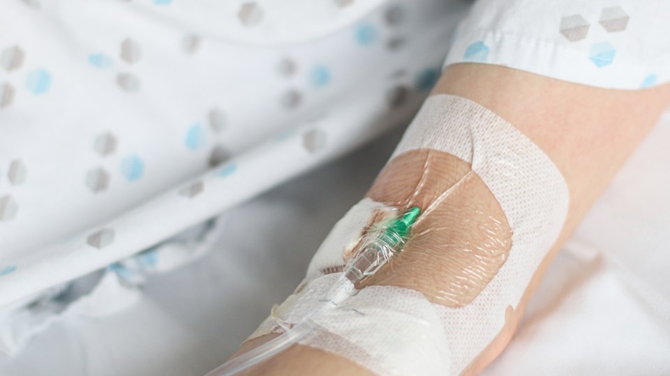 Close up of a patient's arm showing an IV needle affixed with medical tape.